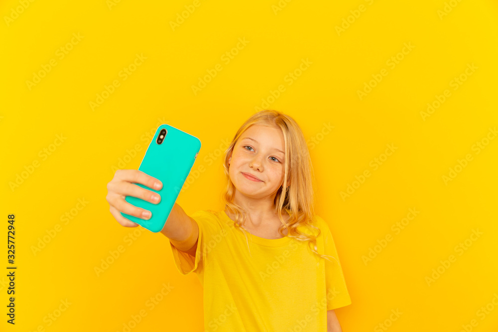 Smiling little girl kid showing blue screen of new popular mobile phone on light yellow background Smiling little girl kid showing blue screen of new popular mobile phone on light yellow background