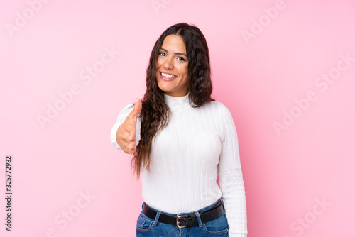 Young woman over isolated pink background shaking hands for closing a good deal