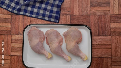Female chef is putting a tray of uncooked chicken legs on wooden table, top view, stock video