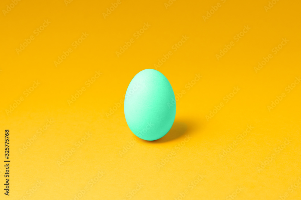 one pastel mint color egg in center on yellow background. easter concept design