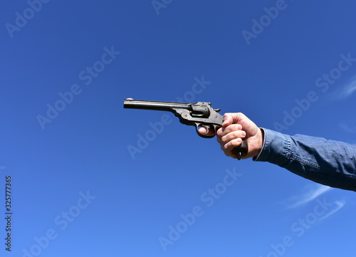 Man holding a .44 or .45 caliber revolver outdoors with blue sky.