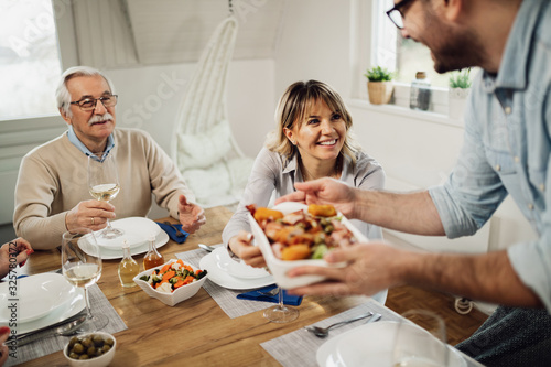 Happy woman talking to her husband who s serving lunch at dining table.