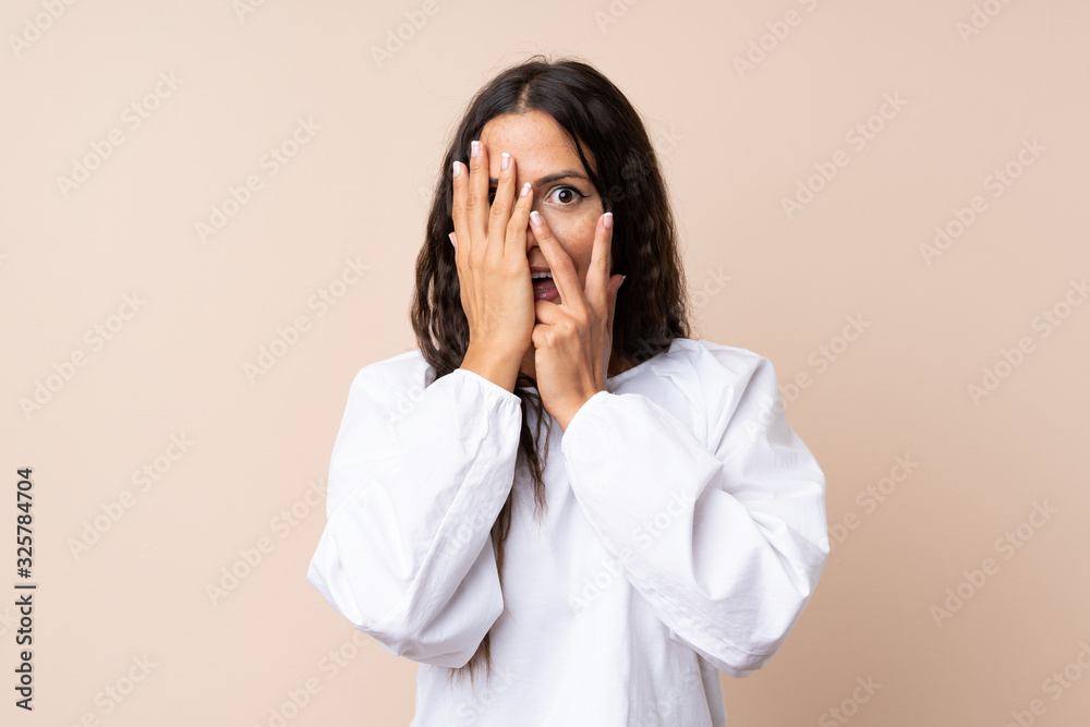 Young woman over isolated background covering eyes and looking through fingers Young woman over isolated background covering eyes and looking through fingers