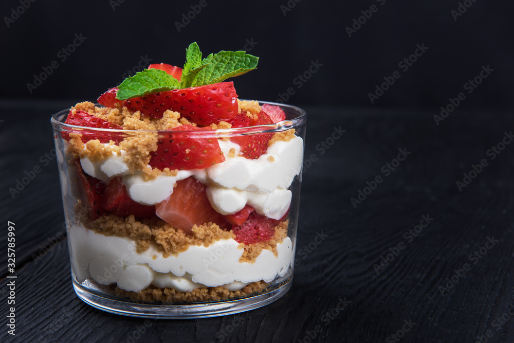 Strawberry with cookie and cream dessert decorated with mint leaf on black wooden background Strawberry with cookie and cream dessert decorated with mint leaf on black wooden background