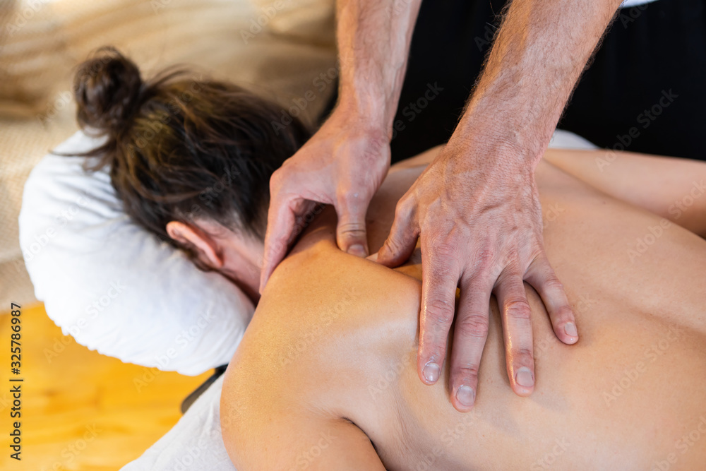 Young female enjoying relaxing back and neck massage in the home. Masseur-therapist doing medical massage of the sore back of the patient Young female enjoying relaxing back and neck massage in the home. Masseur-therapist doing medical massage of the sore back of the patient