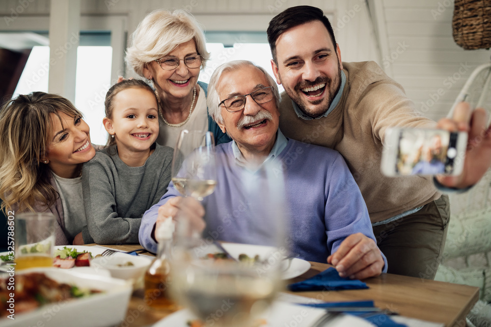 Obraz premium Cheerful multi-generation family taking selfie at dining table.