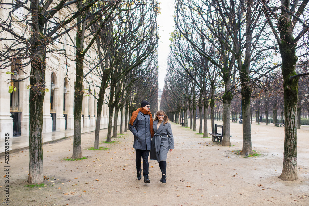 Young beautiful couple dressed stylishly, a girl in a gray coat, a man in a gray coat are walking in a park in Paris France Young beautiful couple dressed stylishly, a girl in a gray coat, a man in a gray coat are walking in a park in Paris France