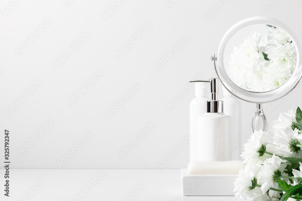 Soft light white bathroom decor, mirror, soap dispenser, white flowers, accessories on white shelf. Elegant decor bathroom interior. - obrazy, fototapety, plakaty 