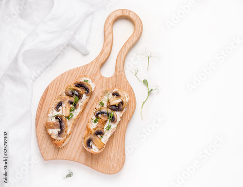 vegetarian sandwich with cheese, fried mushrooms and micro greens on a wooden board on a light background. copy space. close-up