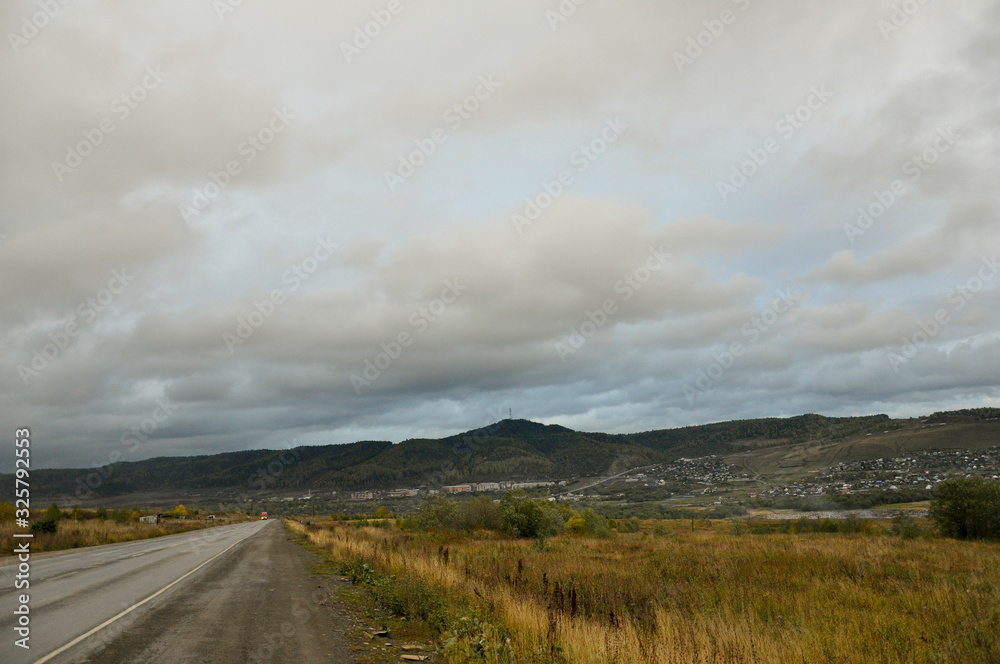 Heavy grey clouds in the cold autumn sky over village with small houses far away in the mountains and fields. Travelling. People living. Roads Heavy grey clouds in the cold autumn sky over village with small houses far away in the mountains and fields. Travelling. People living. Roads