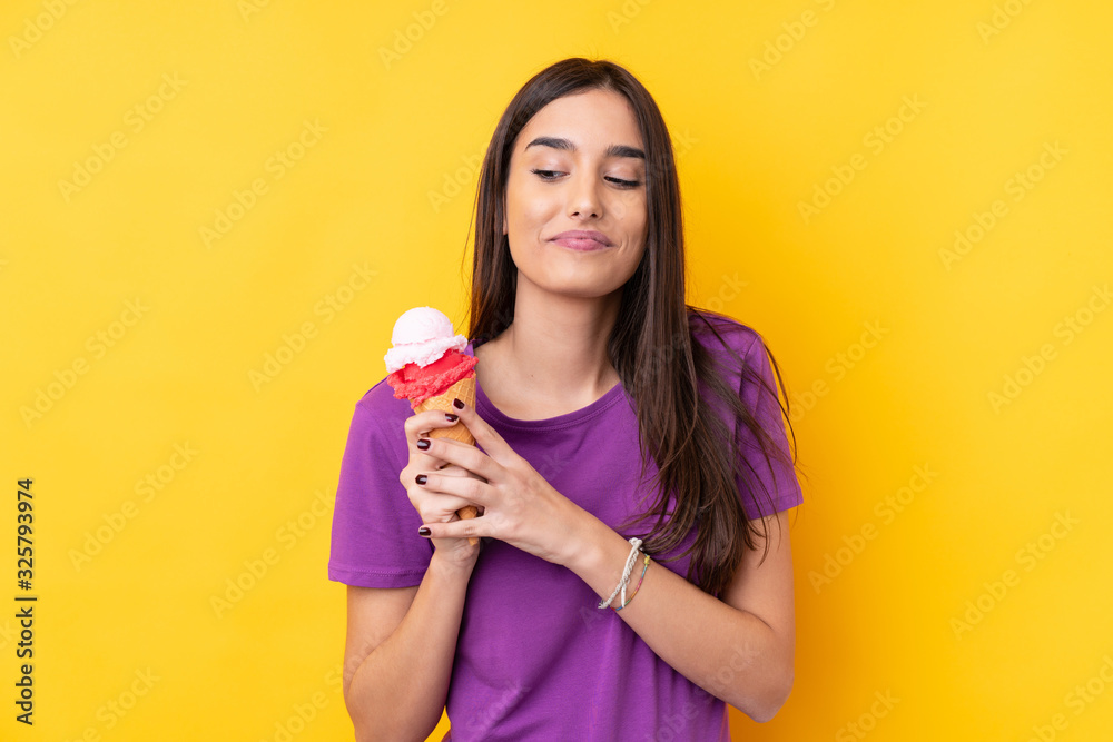 Young brunette woman with a cornet ice cream over isolated yellow background
