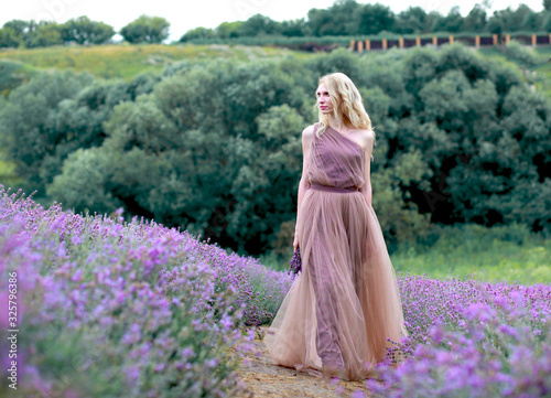 beautiful blonde girl in a light flying dress in a lavender field in summer enjoying her holidays