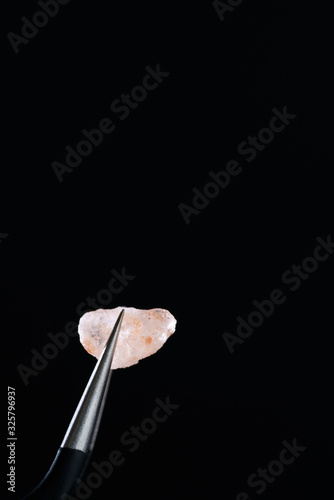 Macro shot of Himalayan salt crystal. Metal tweezers, black background, high resolution, hard light