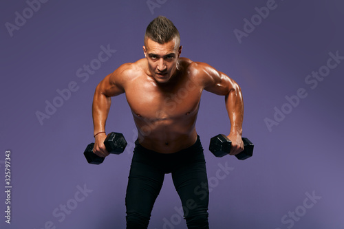 serious bodybuilder lifting heavy dumbbells, looking to camera, man working out at gym, keeping fit, close up portrait, isolated blue background, studio shot, weightlifting, effort, motivation