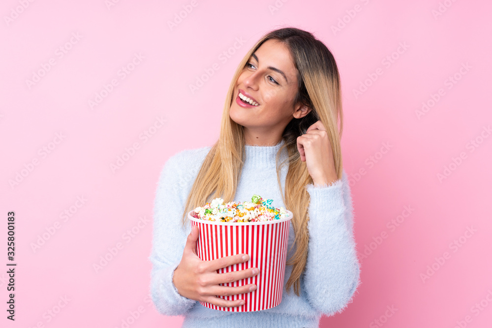 Young Uruguayan woman over isolated pink background holding a big bucket of popcorns Young Uruguayan woman over isolated pink background holding a big bucket of popcorns