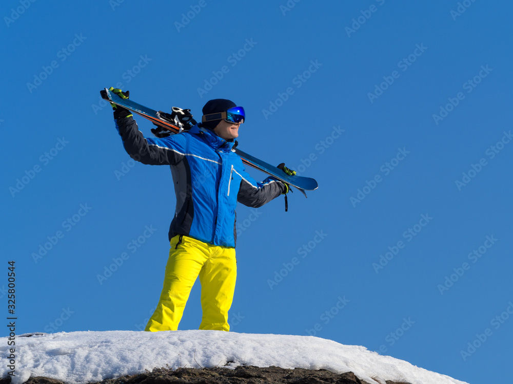 Winter portrait of a man with a ski on a mountain peak over blue sky background. Active lifestyle concept