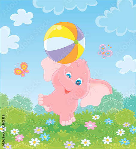 Little pink elephant playing with a big colorful ball on green grass among flowers and flittering butterflies on a summer field on a sunny warm day, vector cartoon illustration