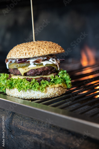 Duży burger ze świeżymi warzywami i serem owinięty w papier ekologiczny. Grillowana kanapka meksykańska na drewnianym stole w stylu industrialnym. Hamburger na wynos z widokiem na ogród.