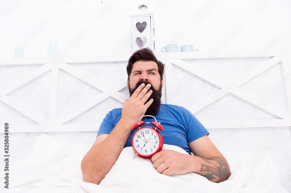 Stressed man yawning takes alarm clock. Too early. Sleepy man holding ...