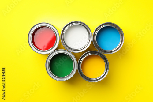Cans of different paints on yellow background, top view