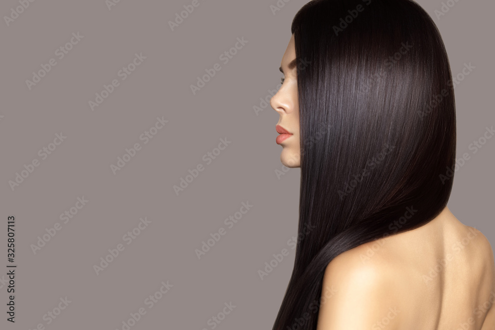 Fototapeta premium Hair care model. Hair cosmetics. Beauty fashion profile portrait of young brunette woman with smooth healthy long hair posing against gray background.