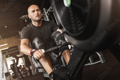 Fitness caucasian young adult man using rowing machine in the gym for fit training