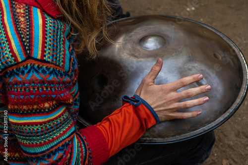 A native musician is seen close up, using hand to beat a hang metal pan drum outdoors during a festival celebrating traditional culture and earth photo