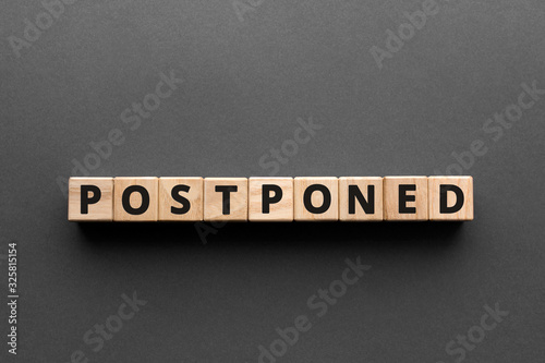Postponed - words from wooden blocks with letters, postponed concept, top view gray background