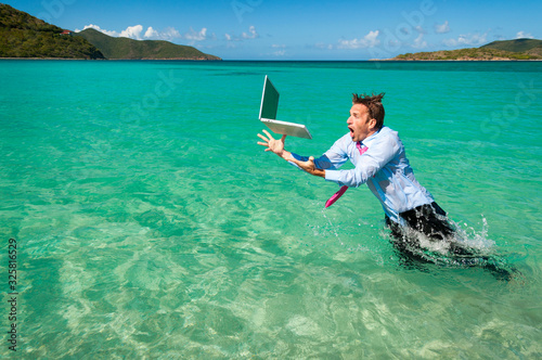 Shocked office worker leaping out of the water to catch his falling laptop computer in bright blue tropical sea