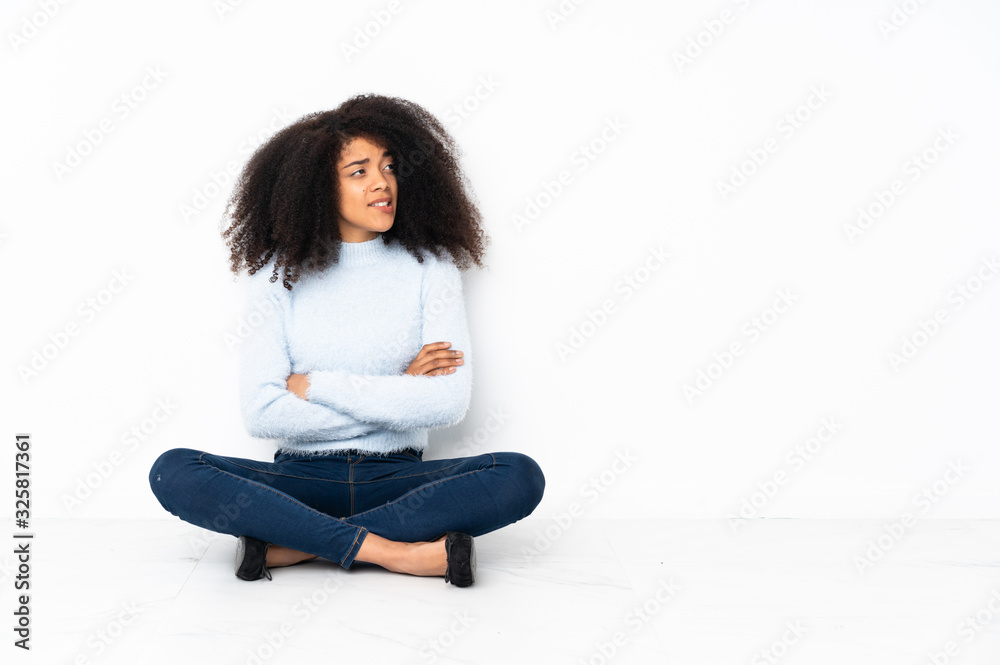 Young african american woman sitting on the floor with confuse face expression