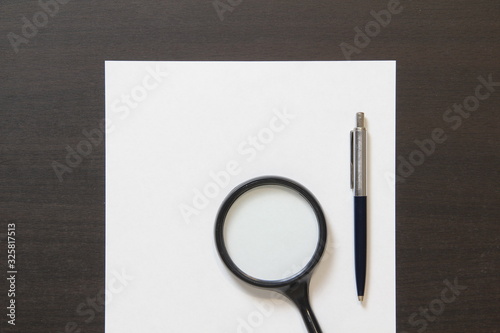 Template of white paper with pen and magnifier on dark wenge color wooden background.