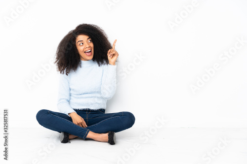 Young african american woman sitting on the floor intending to realizes the solution while lifting a finger up