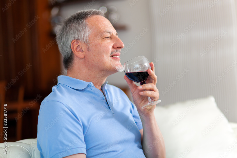 Handsome senior man sitting on couch and enjoying perfect wine taste and aroma Handsome senior man sitting on couch and enjoying perfect wine taste and aroma