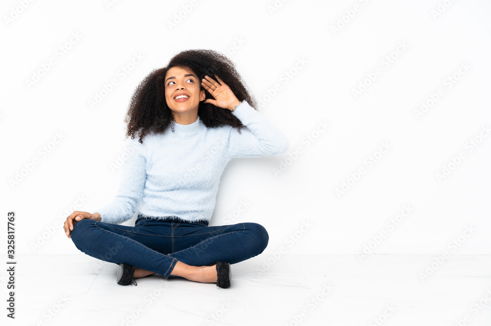 Young african american woman sitting on the floor listening to something by putting hand on the ear Young african american woman sitting on the floor listening to something by putting hand on the ear