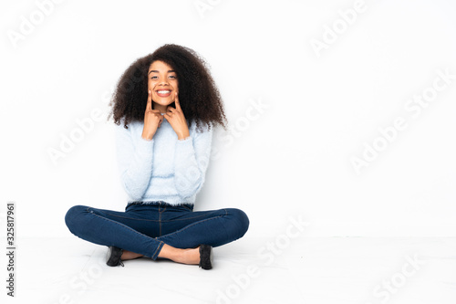 Young african american woman sitting on the floor smiling with a happy and pleasant expression