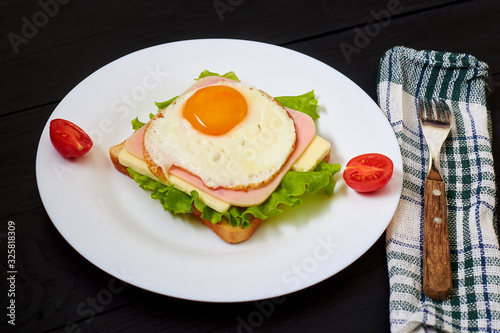 Toast with ham  egg and tomato on a plate on a black background.