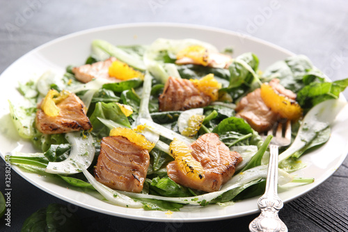 Leafy salad with red fried fish and orange on a white plate with a fork on a grey background. Background image, copy space