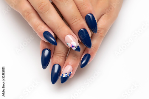 Dark blue manicure on sharp long nails with orchids and white, blue crystals on the ringless fingers. Indigo manicure.