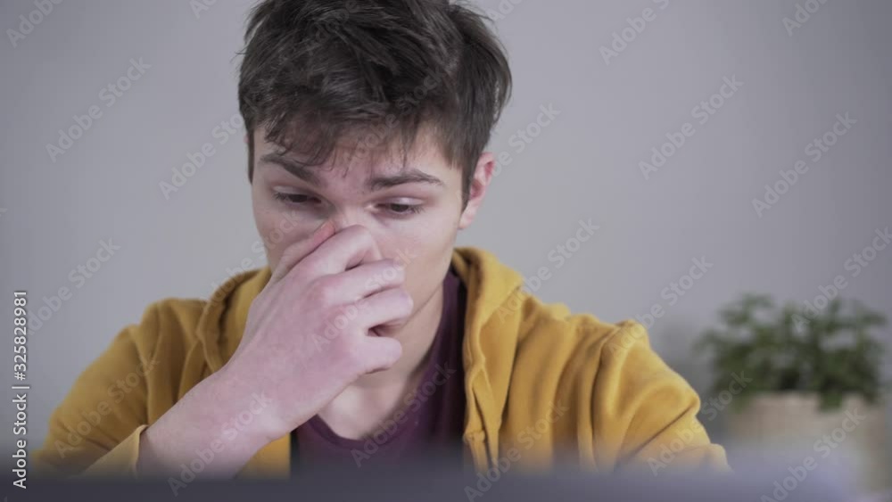 Close-up face of tired Caucasian boy taking off eyeglasses and rubbing nose. Smart serious college student working hard at home. Overload, education, brilliance, intellect. Close-up face of tired Caucasian boy taking off eyeglasses and rubbing nose. Smart serious college student working hard at home. Overload, education, brilliance, intellect.