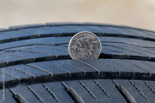Closeup of checking tire tread wear depth of old tire using a quarter coin. Concept of automobile safety, maintenance, and repair