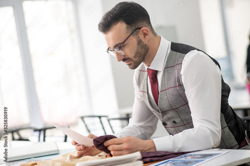 Male tailor sitting, holding pattern and cloth Male tailor sitting, holding pattern and cloth