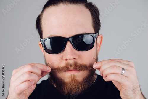 Handsome young man with a beard and mustache in sunglasses in fashionable clothes.