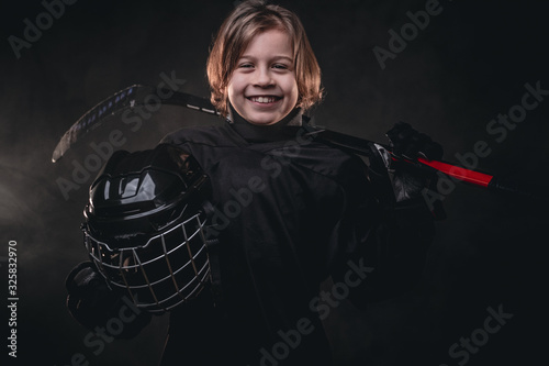 Canvas Print Small blonde sporty boy, ice hockey player, posing in a dark studio for a photos