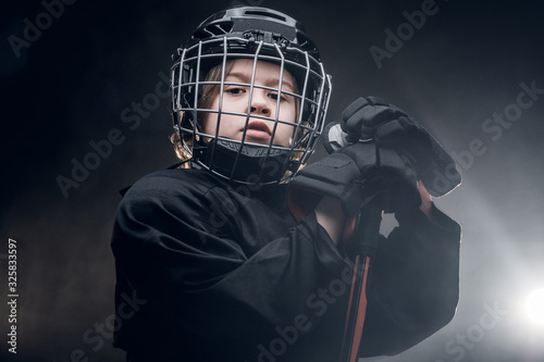 Photography Young blonde sportsman boy, ice hockey player, posing in a dark studio for a pho