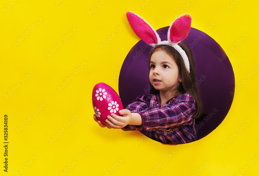 Funny happy child girl with Easter eggs and bunny ears on yellow Funny happy child girl with Easter eggs and bunny ears on yellow