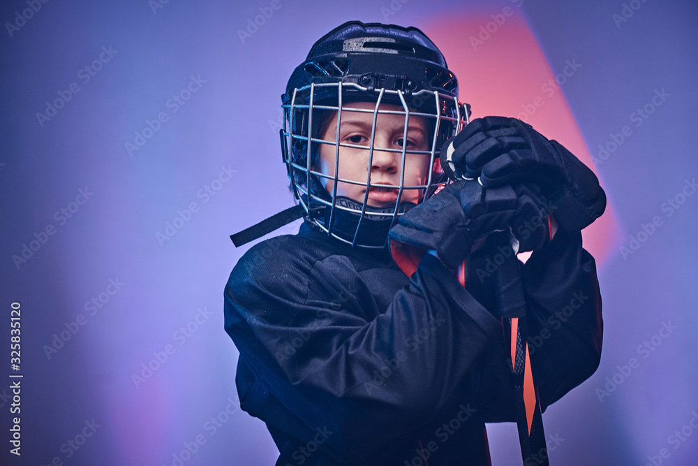 Young blonde fit boy, ice hockey player, posing in a bright neon studio for a photoshoot, wearing an ice-skating uniform while wearing his helmet, holding a hockey stick in his arms and looking Young blonde fit boy, ice hockey player, posing in a bright neon studio for a photoshoot, wearing an ice-skating uniform while wearing his helmet, holding a hockey stick in his arms and looking