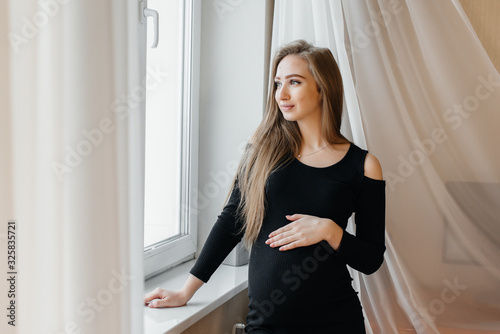 A beautiful pregnant girl is standing in a room near the window