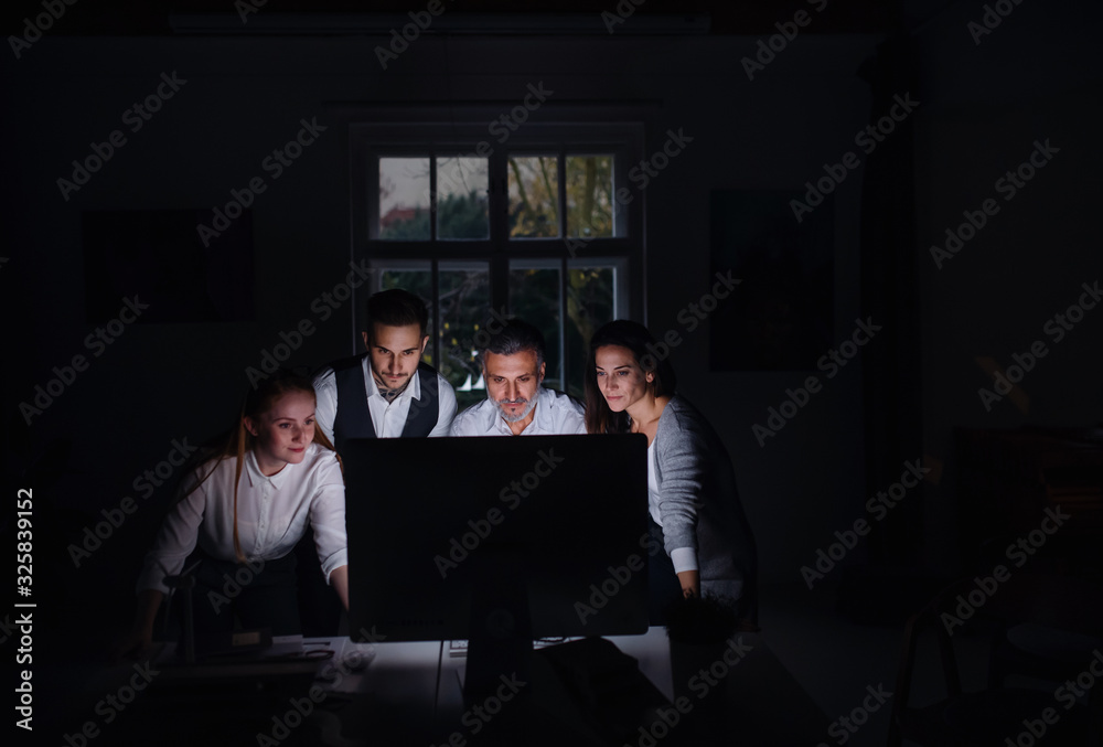 Group of businesspeople with computer indoors in office, working late. Group of businesspeople with computer indoors in office, working late.