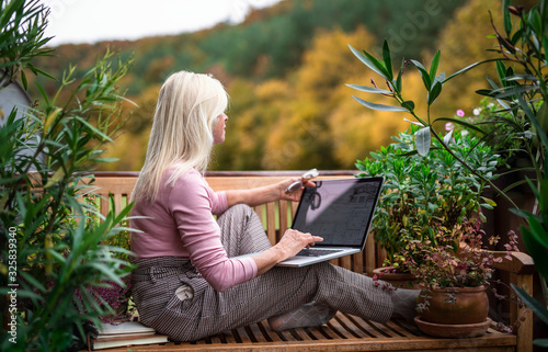 Senior woman architect with laptop sitting outdoors on terrace, working.