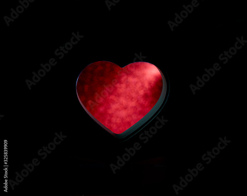 Blurred red out of focus bokeh of shiny red in a hole on a black background in the shape of a heart. Abstract layout any shape horizontally and vertically. glitter boke soft lights.